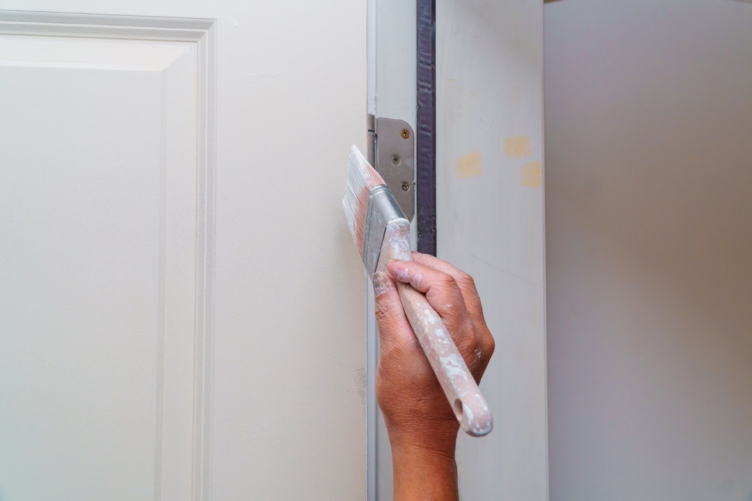 Person painting a door white, ideal option to restyling an already installed door.